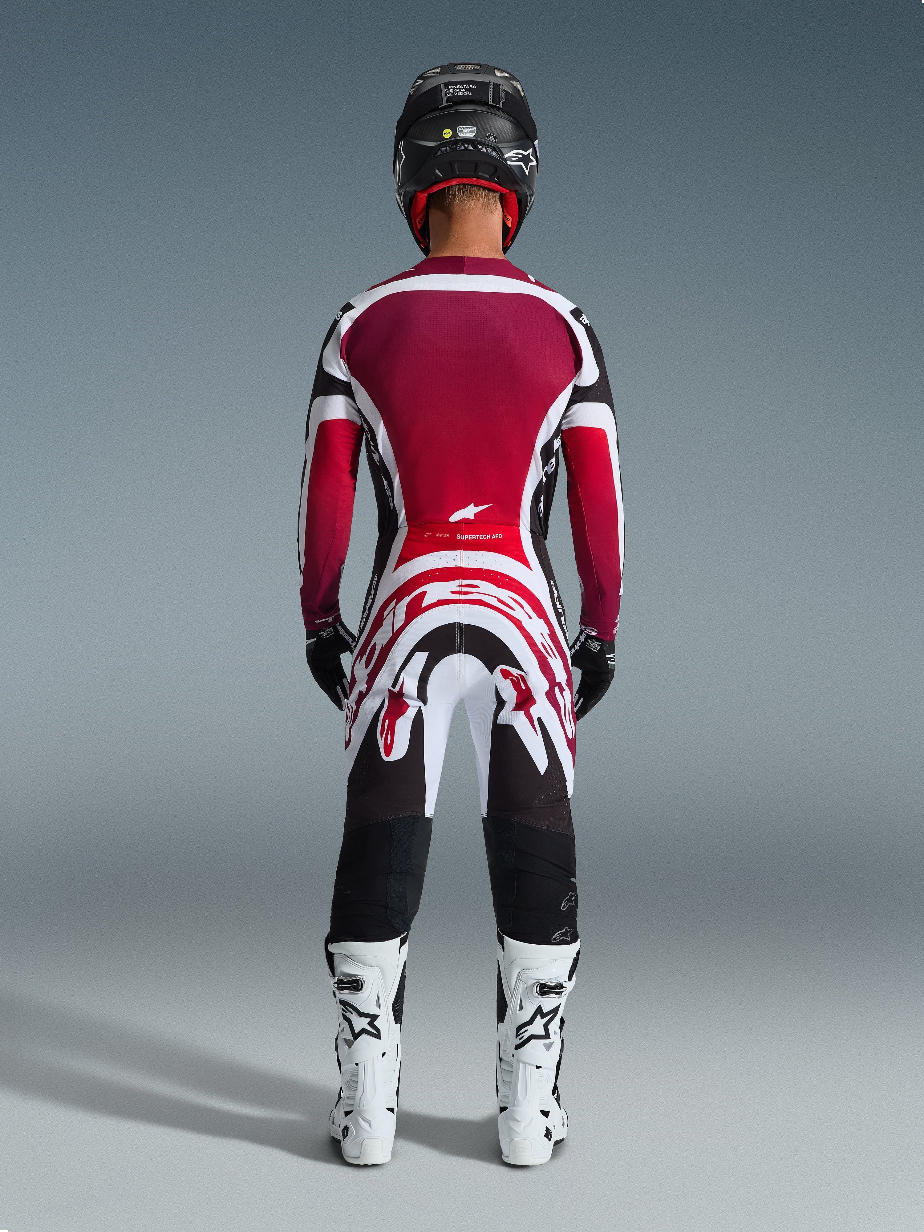 Motocross rider from behind wearing the 2026 Supertech AFD Vista Jersey in Black, Red, and White, paired with matching motocross pants, black helmet, and white boots, complete professional racing gear set for off-road competition