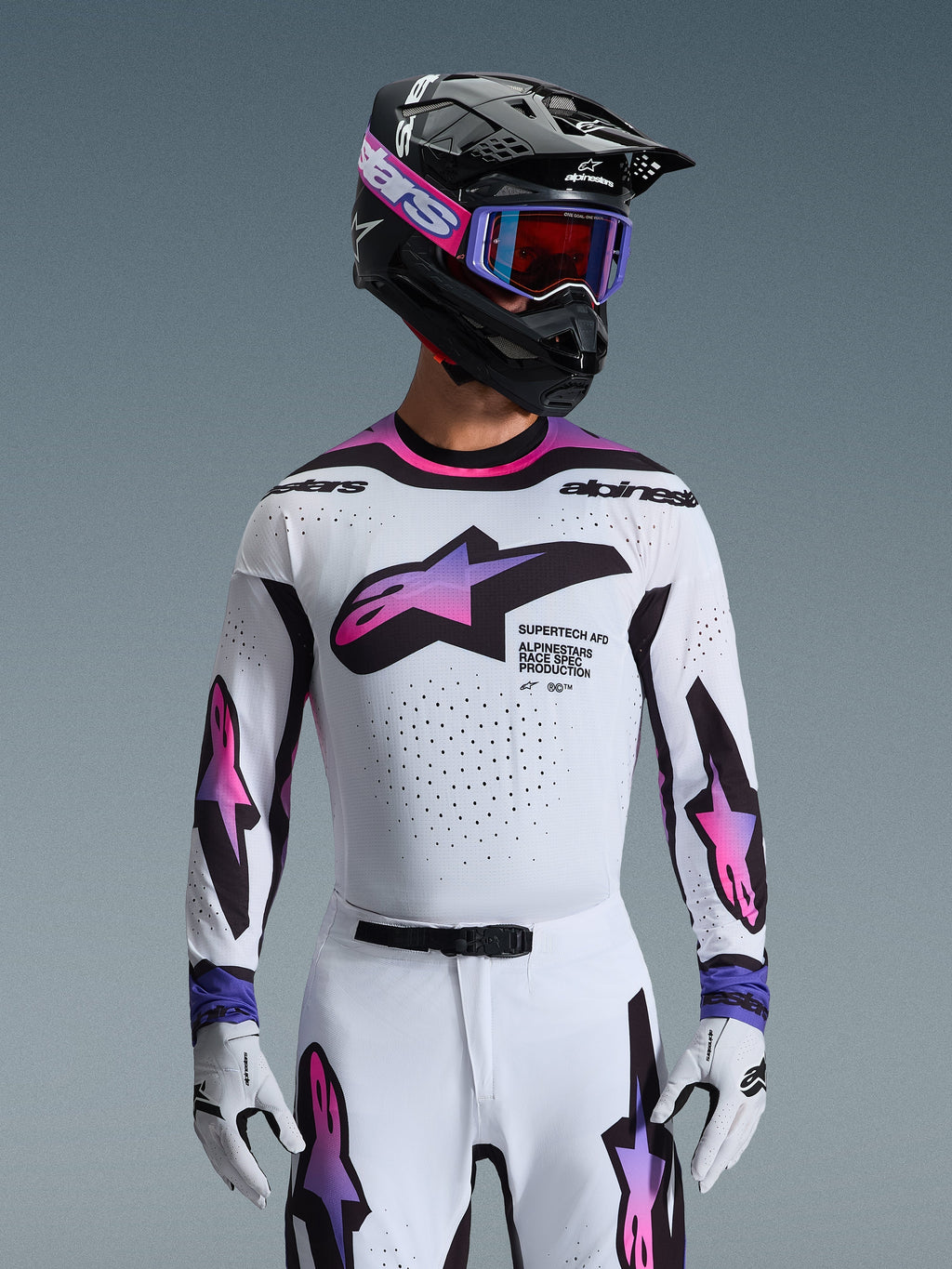 Motocross-Fahrer im 2026 Supertech AFD Vista Trikot in Weiß, Lila und Schwarz, mit schwarzem Helm mit pinkfarbenem Branding, lila Goggle und passenden weißen Handschuhen, athletische Passform für professionelle Offroad-Rennperformance