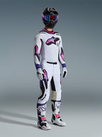 Motocross rider wearing the 2026 Supertech AFD Vista Gear Set, White jersey with purple and pink star logos, matching white pants with black accents, black helmet with purple goggles, and white boots with pink details, professional off-road racing outfit