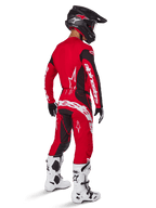 Motocross rider wearing the Alpinestars 2025 Techstar Dreem Gear Set in Bright Red and Black, featuring white branding on the jersey and pants, paired with a black helmet, white and black boots, and black and white gloves, rear three-quarter view.