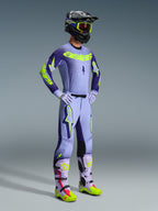 Motocross rider wearing the 2026 Supertech Scenz Jersey and full racing kit, Purple and Yellow Fluo design with light purple base and neon accents, matching pants with bold star logos, black helmet with neon yellow goggles, coordinated purple and neon yellow boots, professional off-road gear set.