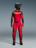 Motocross rider wearing the Alpinestars 2026 Supertech Scenz Jersey in Red Black Yellow, styled with matching pants, black helmet with goggles, red gloves, and black and red boots, professional racing gear set for off-road performance