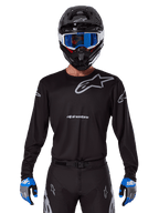 Alpinestars 2025 Racer Graphite Jersey, Motocross Racing Gear, Black with Gray logos, worn with matching black helmet, blue goggles, and blue and gray gloves, form-fitting performance design with chest and arm branding
