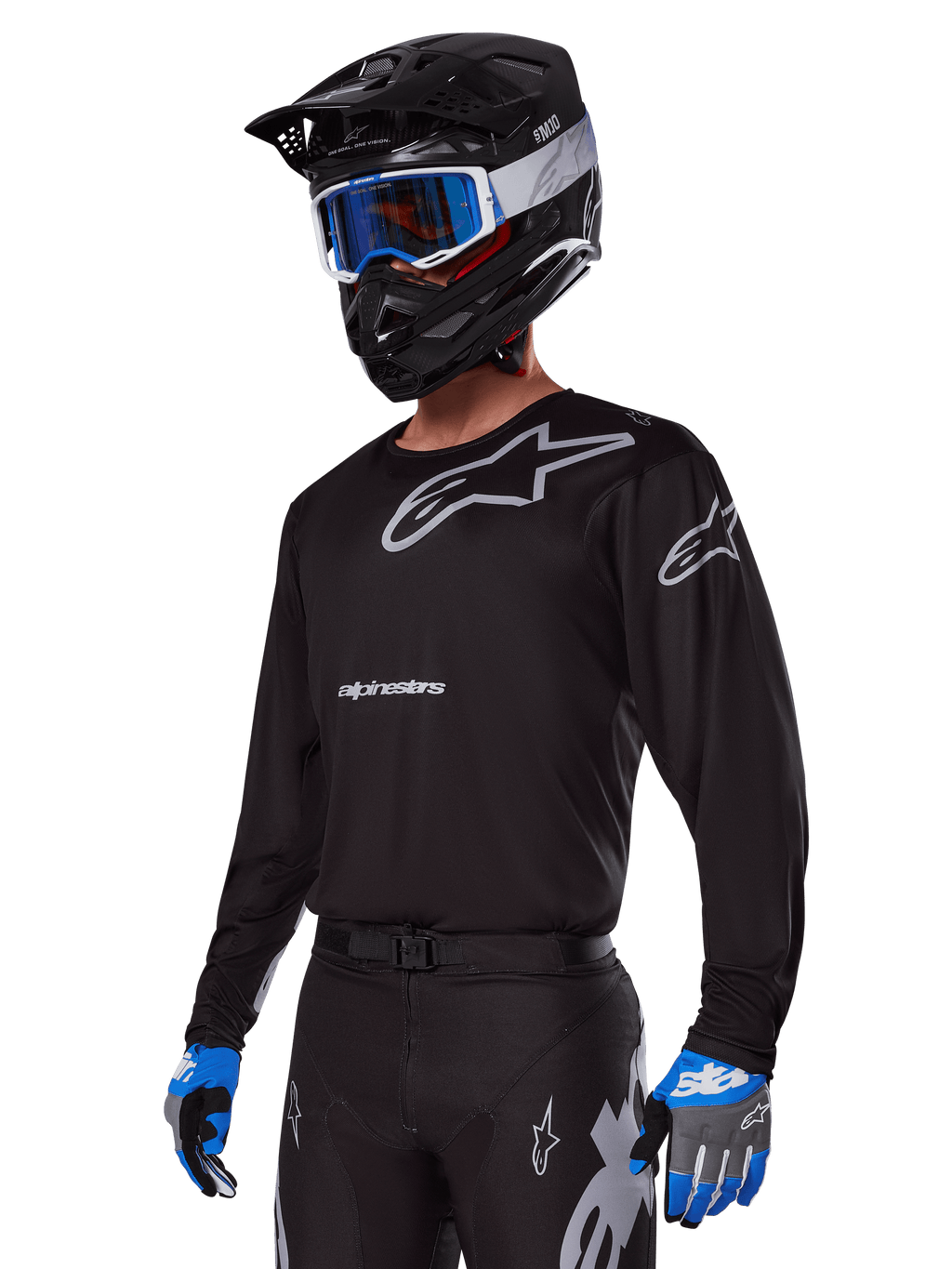 Motocross-Fahrer im Alpinestars 2025 Racer Graphite Ausrüstungsset, schwarzes Jersey mit grauen Alpinestars-Logos, passende schwarze Hose mit grauen Akzenten, schwarzer Helm mit blau-weißer Brille, blau-graue Handschuhe, elegantes technisches Outfit für Offroad-Rennsport