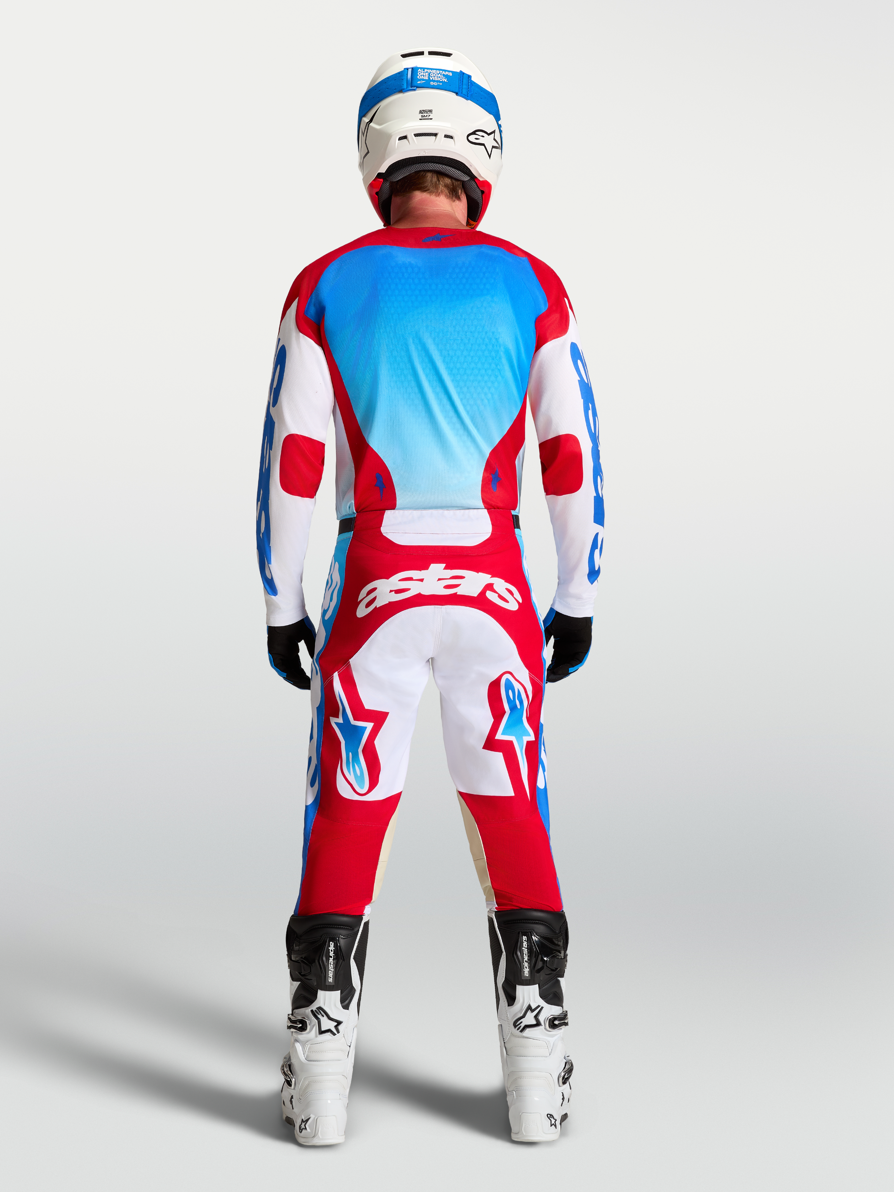 Alpinestars Racer Hose Hunt und Racer Hunt Gear Set, Motocross-Ausrüstung in Rot, Weiß und Blau, Rückansicht am Model mit Helm und Motorradstiefeln.