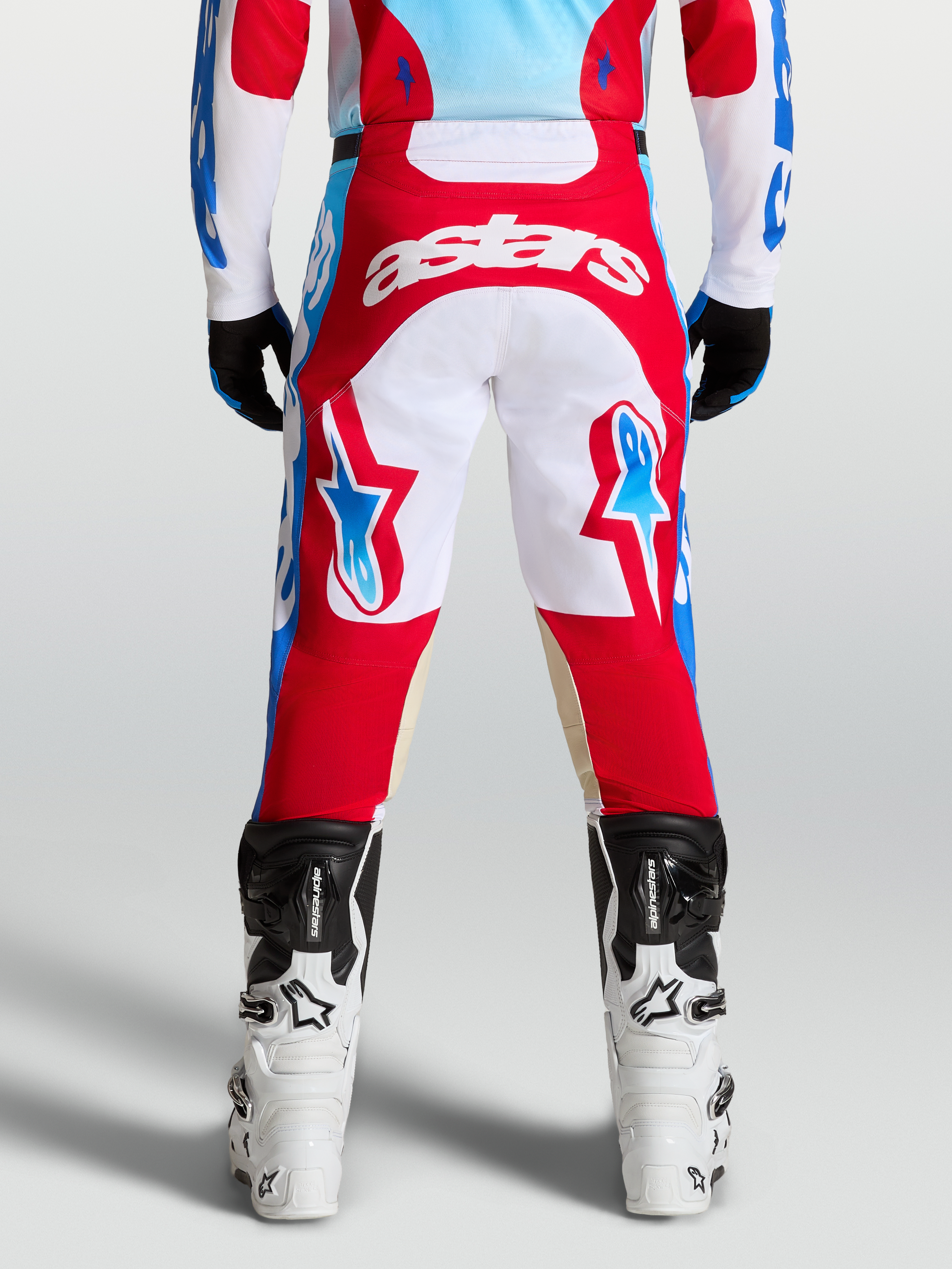 Alpinestars Racer Hose Hunt, Rot und Weiß, Motocross-Hose in der Rückansicht, vorgekrümmte Beinkonstruktion mit hellblauen Akzenten, getragen mit weißen Stiefeln.
