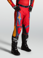 Alpinestars Racer Hunt Hose, Motocross-Hose für Herren, Rot mit grauen und korallenfarbenen Akzenten, am Model mit schwarzen Stiefeln.