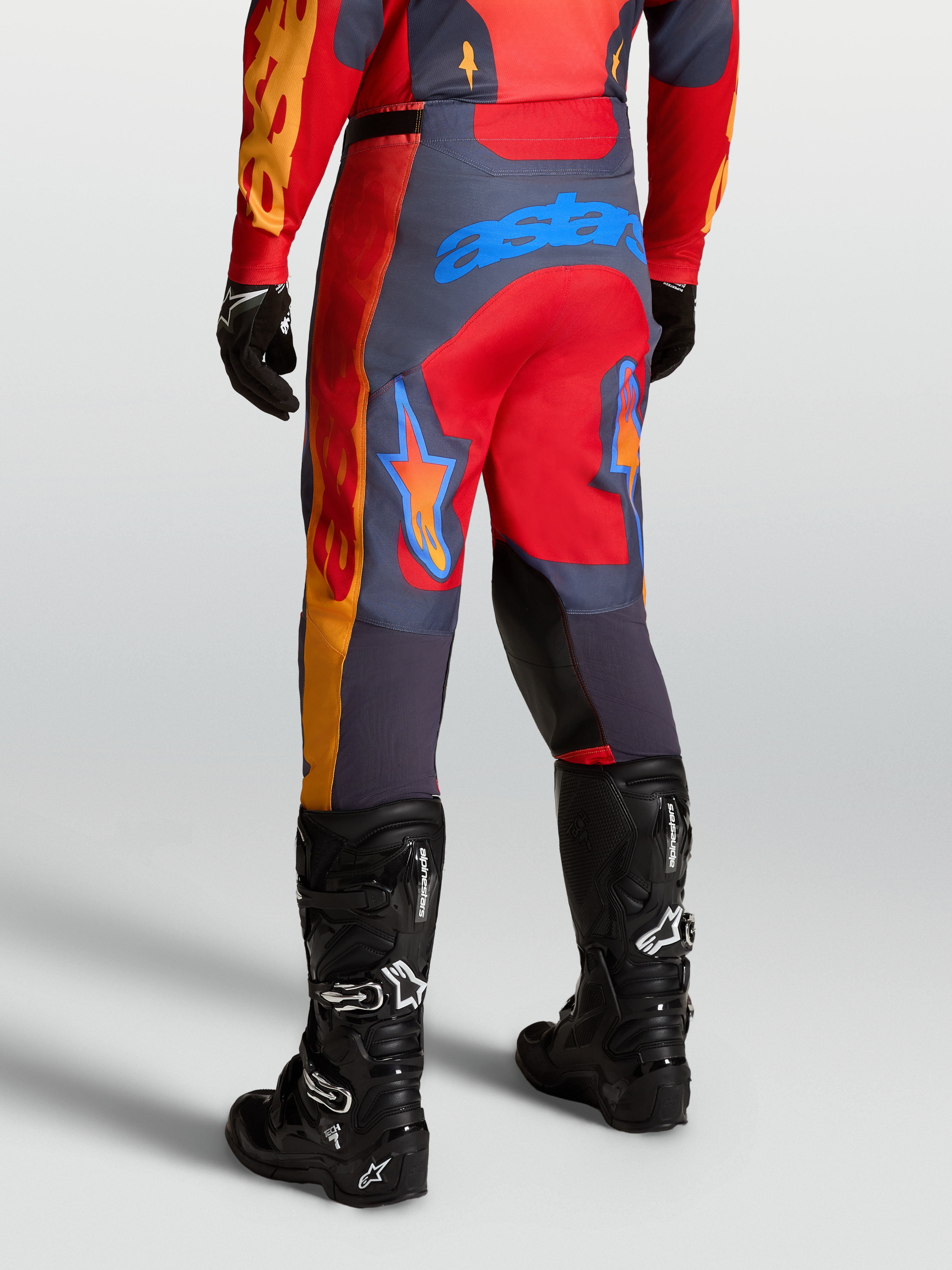 Alpinestars Racer Hunt Hose, Motocross-Performance-Hose in Rot und Grau, Rückansicht in Fahrposition mit schwarzen Tech 7 Stiefeln.