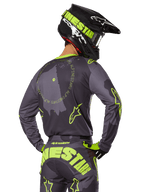 Motocross-Fahrer in der Rückansicht im 2025 Racer Hollow Gear Set, graues Trikot mit neongelbem kreisförmigem Text und Stern-Logos, passende grau-gelbe Hose mit markantem Branding auf dem Gesäß, schwarz-limonengrüner Helm, abgestimmtes Outfit für den Offroad-Rennsport