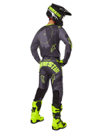 Motocross-Fahrer in der Rückansicht im Alpinestars 2025 Racer Hollow Trikot und der Hose in Dark Camo Yellow Fluo, mit einem dunkelgrauen Camouflage-Muster und neongelben Akzenten, kombiniert mit einem passenden schwarz-gelben Helm und leuchtend neongelben Stiefeln.