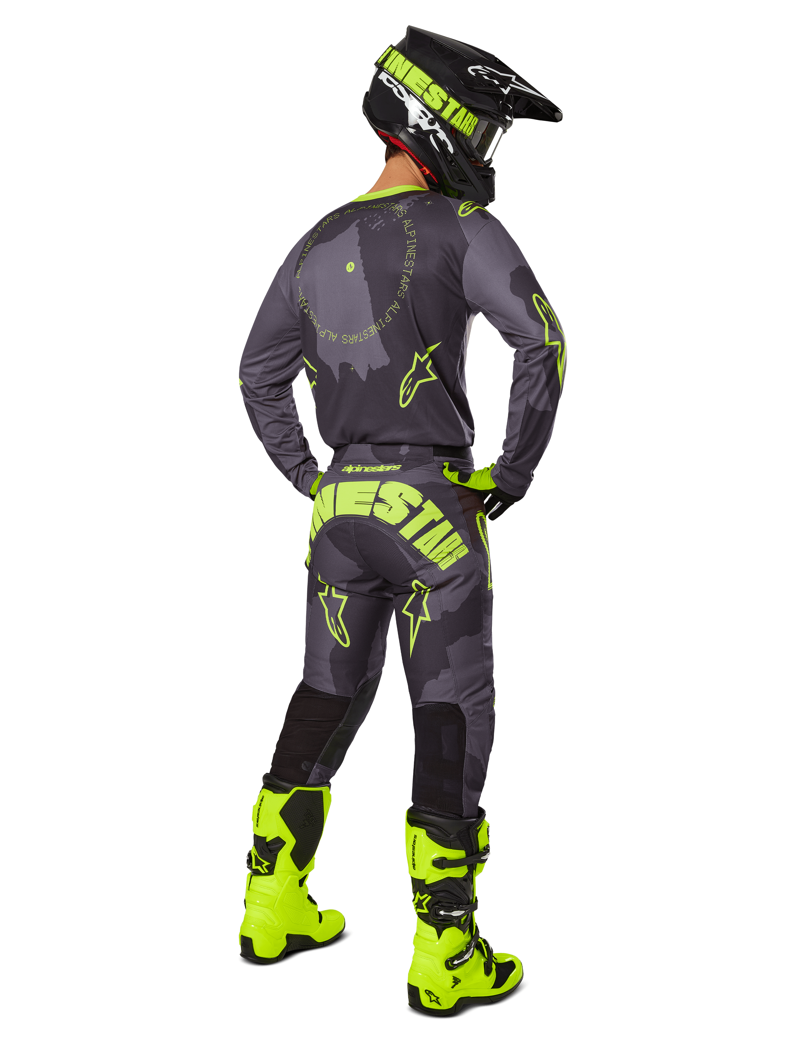 Motocross-Fahrer in der Rückansicht im Alpinestars 2025 Racer Hollow Trikot und der Hose in Dark Camo Yellow Fluo, mit einem dunkelgrauen Camouflage-Muster und neongelben Akzenten, kombiniert mit einem passenden schwarz-gelben Helm und leuchtend neongelben Stiefeln.