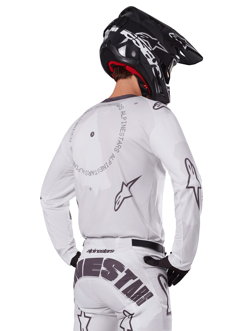 Motocross-Fahrer in der Rückansicht trägt das Alpinestars 2025 Racer Hollow Gear Set in Weiß, weißes Langarmtrikot mit grauen Sternlogos und kreisförmigen Grafiken, passende weiße Hose mit markantem Branding am Gesäß, schwarzer Helm, abgestimmte Offroad-Rennausrüstung.