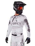 Alpinestars 2025 Racer Hollow Gear Set, Motocross-Trikot und -Hose, Weiß mit schwarzen und grauen Grafiken, mit 'ASTARS'-Branding und hohlen Globus-Designs, getragen mit schwarzem Helm, rot verspiegelter Brille und schwarzen Handschuhen, konzipiert für Offroad-Performance