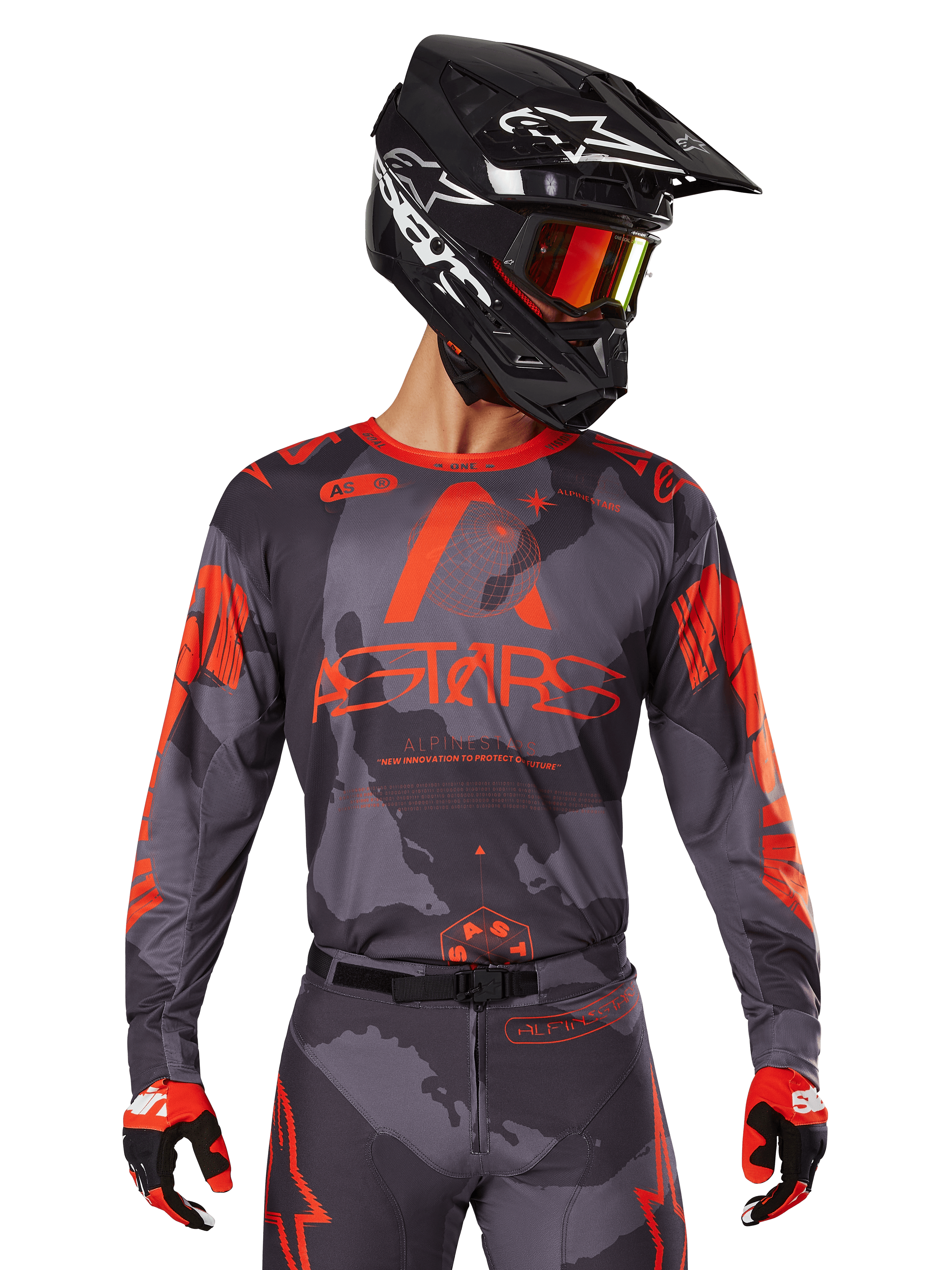 Alpinestars 2025 Racer Hollow Jersey, Motocross-Trikot, Gray Camo und Orange Fluo, getragen mit passendem Ausrüstungsset inklusive Hose und Handschuhen, schwarzer Helm mit weißen Grafiken und Schutzbrille, markantes ASTARS-Branding, schützende Offroad-Rennsportbekleidung