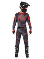 Motocross-Fahrer mit Alpinestars 2025 Racer Hollow Trikot und passender Hose in Grau Camo Orange Fluo, komplette Ausrüstung mit schwarzem Helm, Goggles, Handschuhen und Stiefeln, markante orangefarbene Logos und Camouflage-Muster.