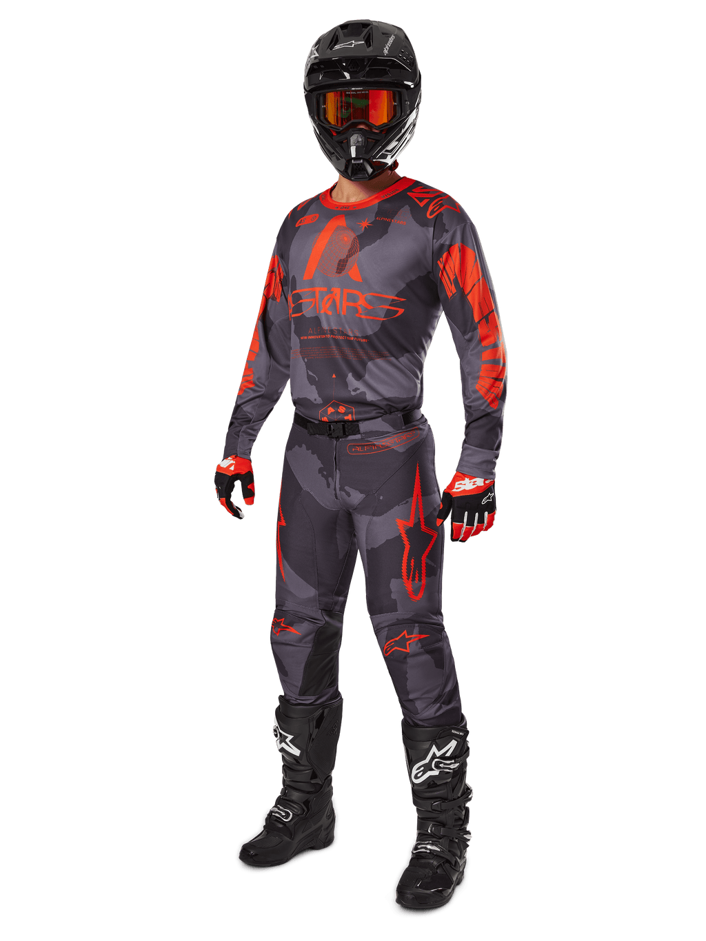 Motocross-Fahrer in kompletter Rennausrüstung, Alpinestars 2025 Racer Hollow Trikot und Hose in Grau Camo Orange Fluo, schwarzer Helm mit orangefarbener Brille, schwarz-rote Handschuhe und schwarze Stiefel mit weißen Logos, abgestimmtes Performance-Outfit für den Offroad-Rennsport