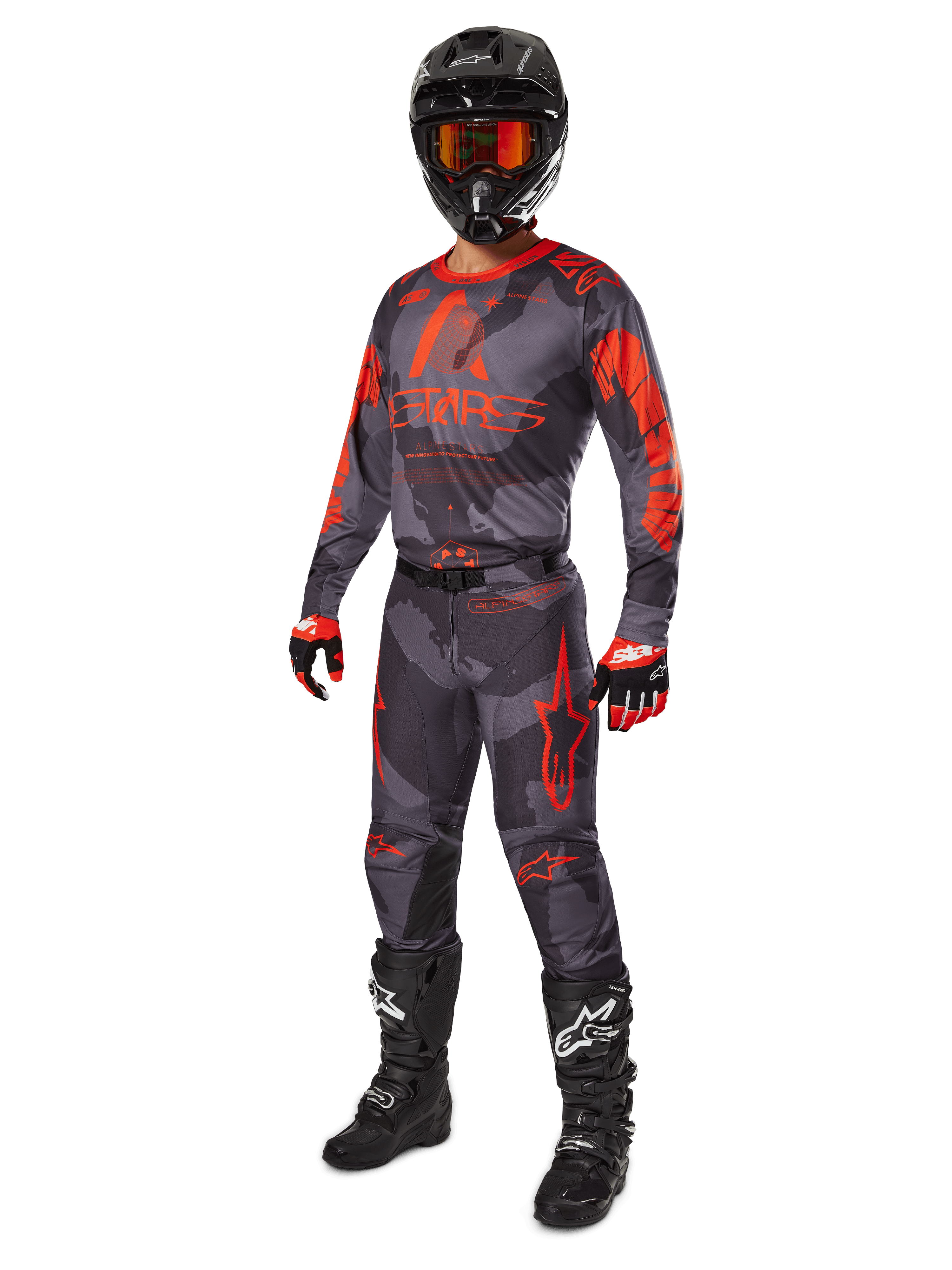 Motocross-Fahrer in kompletter Rennausrüstung, Alpinestars 2025 Racer Hollow Trikot und Hose in Grau Camo Orange Fluo, schwarzer Helm mit orangefarbener Brille, schwarz-rote Handschuhe und schwarze Stiefel mit weißen Logos, abgestimmtes Performance-Outfit für den Offroad-Rennsport
