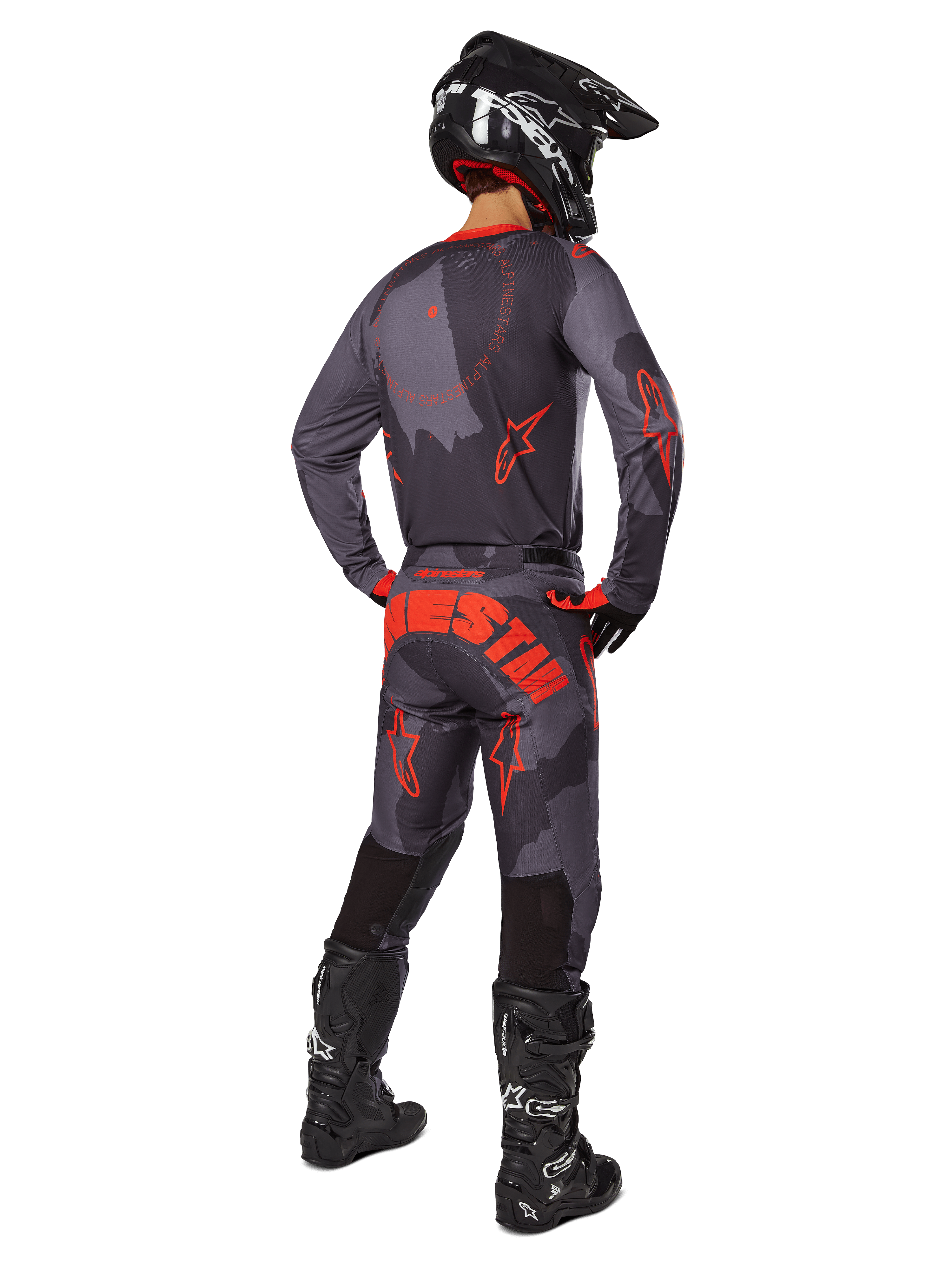 Motocross-Fahrer in der Rückansicht, Alpinestars 2025 Racer Hollow Trikot in Gray Camo Orange Fluo, passende Camo-Hose mit orangem Alpinestars-Schriftzug, schwarzer Helm und schwarze Stiefel, abgestimmtes Ausrüstungsset für Offroad-Fahrten