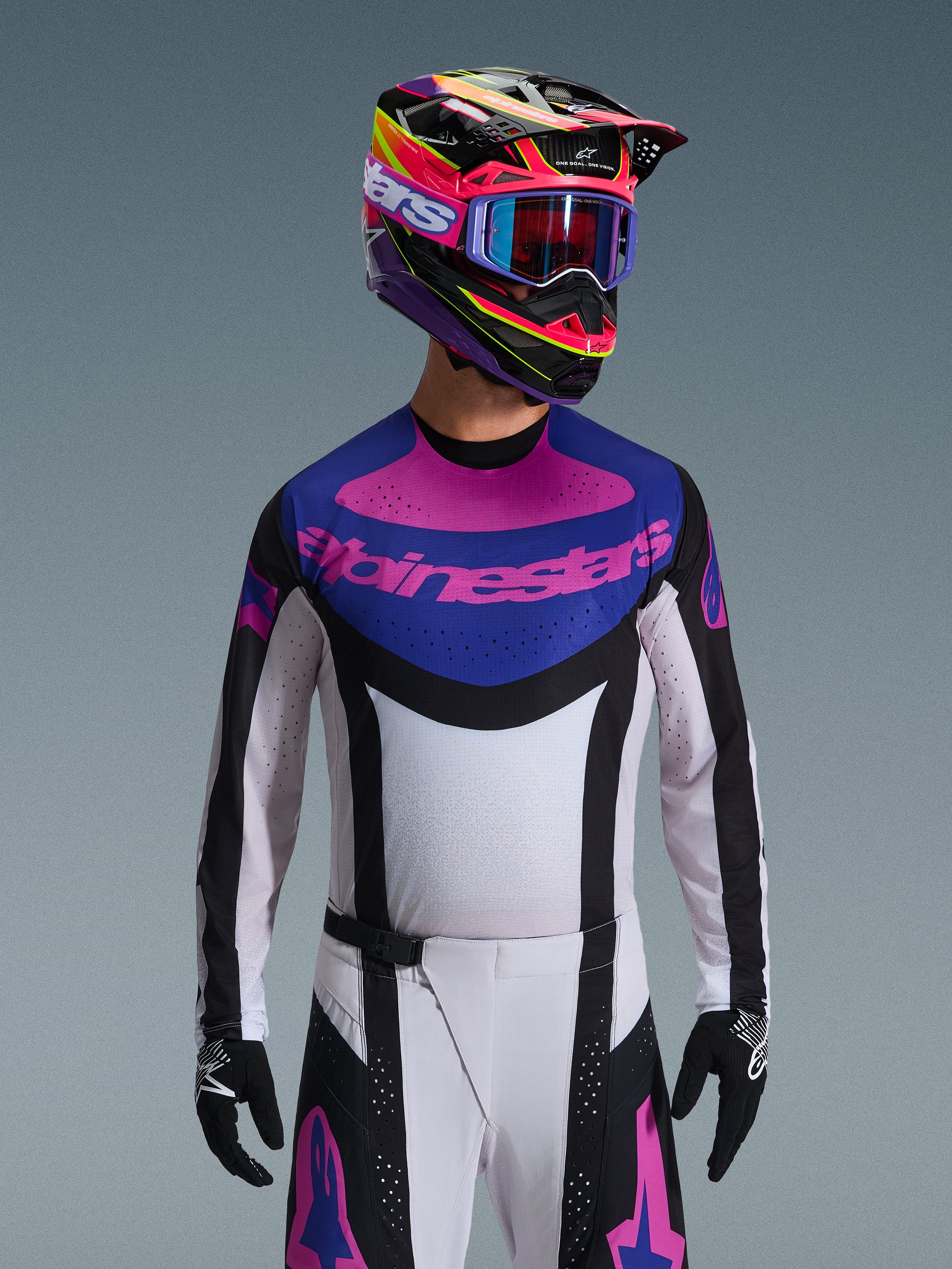 Alpinestars 2026 Techstar Knif Jersey, Motocross-Trikot, Schwarz, Hellgrau und Lila, pinkfarbenes Alpinestars-Logo auf der Brust, getragen mit passendem bunten Helm und Motocross-Hose, athletische Rennpassform mit lasergeschnittenen Perforationen zur Belüftung