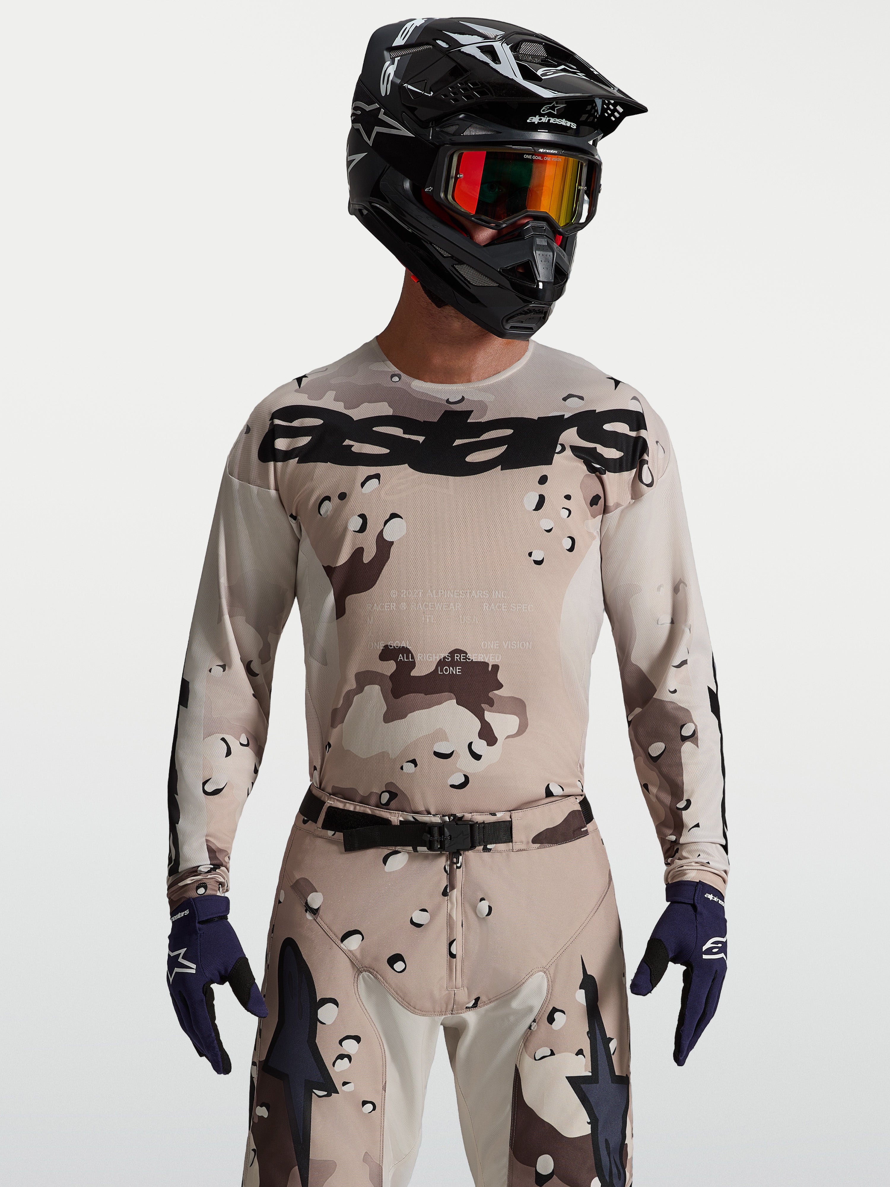 Alpinestars Racer Lone Trikot in Desert Camo und Schwarz, Herren-Motocross-Ausrüstung an Model mit Helm und Schutzbrille.