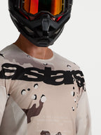 Alpinestars Racer Lone Trikot, Herren-Motocross-Trikot, Desert-Camo und Schwarz, leichtes Polygewebe, Nahaufnahme am Model mit Helm.