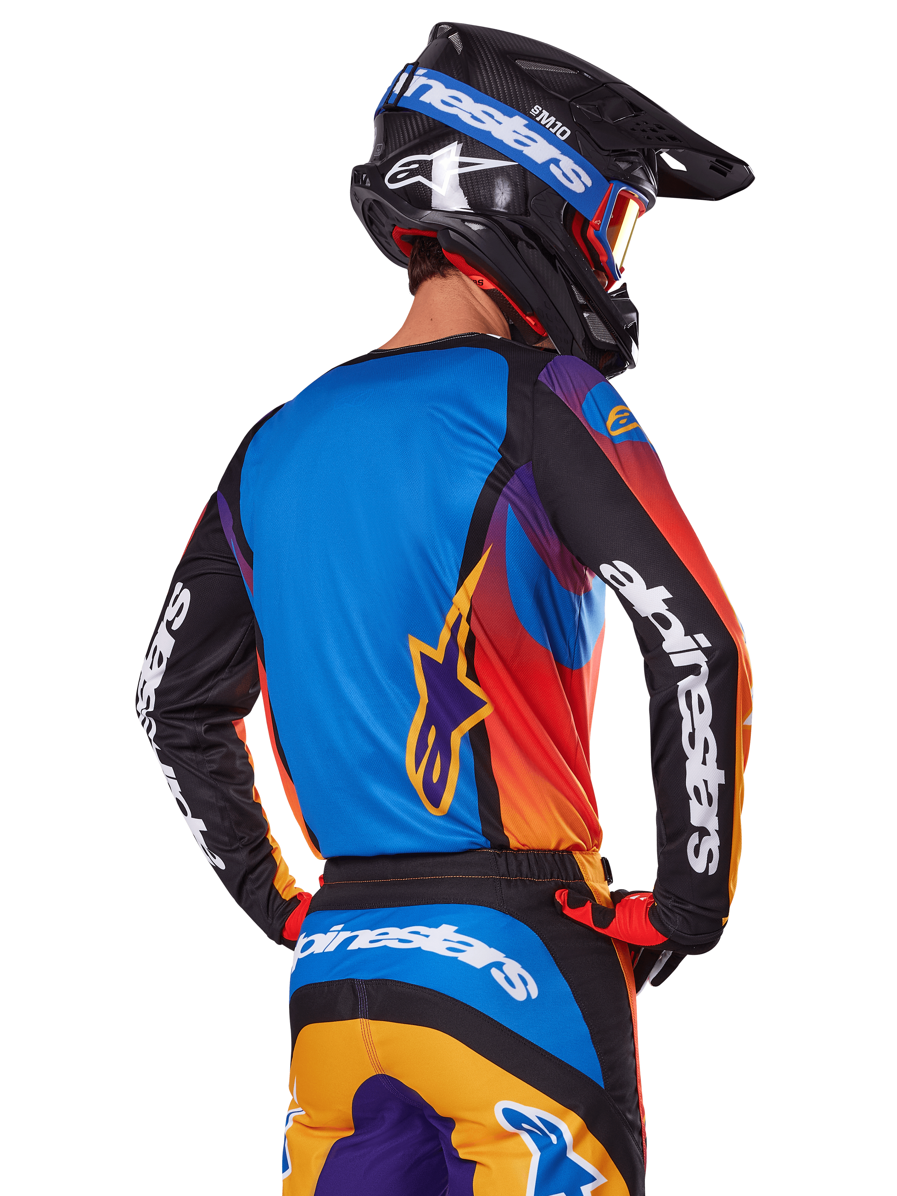 Motocross-Fahrer in der Rückansicht, Alpinestars 2025 Fluid Wurx Ausrüstungsset, mehrfarbiges Trikot mit blauem Rücken und schwarzen Ärmeln mit weißen Logos, passende orange-blaue Hose, schwarz-blauer Helm mit orangefarbener Schutzbrille, koordiniertes Offroad-Rennoutfit.