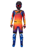 Motocross-Fahrer im Alpinestars 2025 Fluid Wurx Ausrüstungsset, mit lebhaftem Farbverlauf in Orange, Gelb und Blau auf Trikot und Hose, schwarzen Alpinestars-Logos, blauen Rennstiefeln, rot-schwarzen Handschuhen und schwarzem Helm mit roter Brille, abgestimmte Komplettausrüstung für den Offroad-Rennsport