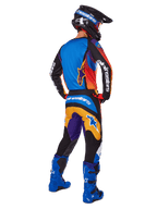 Motocross-Fahrer in der Rückansicht mit Alpinestars 2025 Fluid Wurx Gear Set, mehrfarbiges Trikot mit blauen, orangefarbenen und lila Paneelen, passende Hose mit weißem Alpinestars-Logo auf dem Gesäß, leuchtend blaue Stiefel und schwarzer Helm, koordiniertes Outfit für den Offroad-Rennsport
