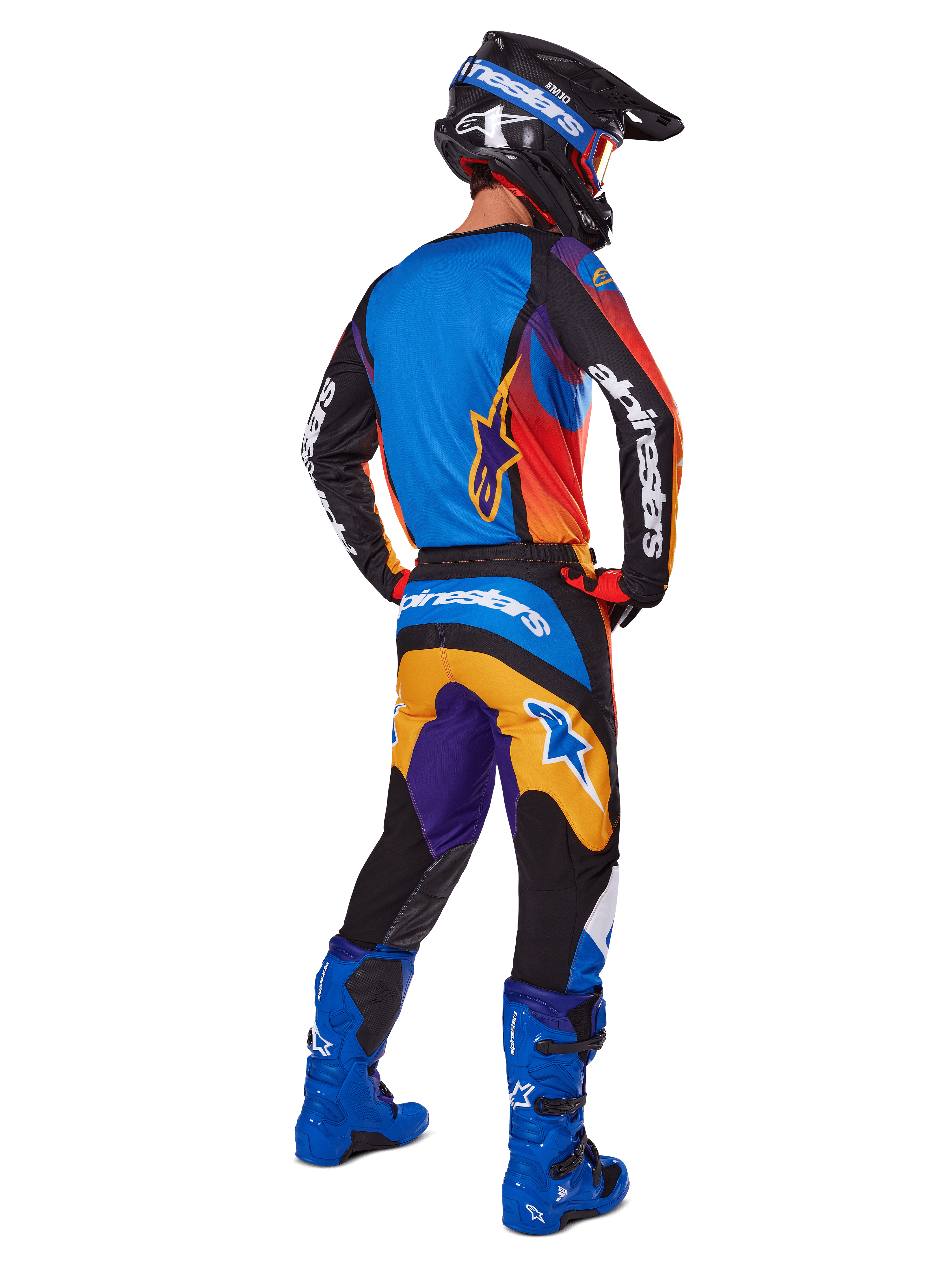 Motocross-Fahrer in der Rückansicht mit Alpinestars 2025 Fluid Wurx Gear Set, mehrfarbiges Trikot mit blauen, orangefarbenen und lila Paneelen, passende Hose mit weißem Alpinestars-Logo auf dem Gesäß, leuchtend blaue Stiefel und schwarzer Helm, koordiniertes Outfit für den Offroad-Rennsport