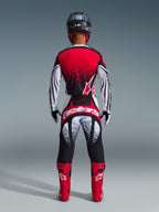 Motocross rider from behind wearing the Alpinestars 2026 Techstar Nomur Jersey, Red Black and White with stippled pattern, matching racing pants, red motocross boots and black helmet, complete gear set for off-road competition