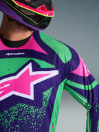 Close-up of Alpinestars 2026 Techstar Nomur Jersey, Deep Purple with Green and Pink Fluo accents, featuring a large pink star logo on the chest and laser-cut perforations on the shoulder, worn by a rider with a matching purple and pink motocross helmet.