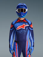 Alpinestars 2026 Techstar Nomur Jersey, Motocross Racing Jersey, Dark Navy, Orange, and UCLA Blue, worn with matching pants, blue helmet, and gloves, featuring a white star logo on the chest with dynamic lines and speckled patterns