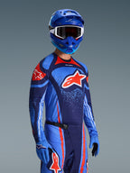 Alpinestars 2026 Techstar Nomur Gear Set, Motocross Jersey and Pants in Dark Navy, Orange, and UCLA Blue, worn by a rider with matching blue helmet and gloves, featuring bold logo graphics and athletic race fit.