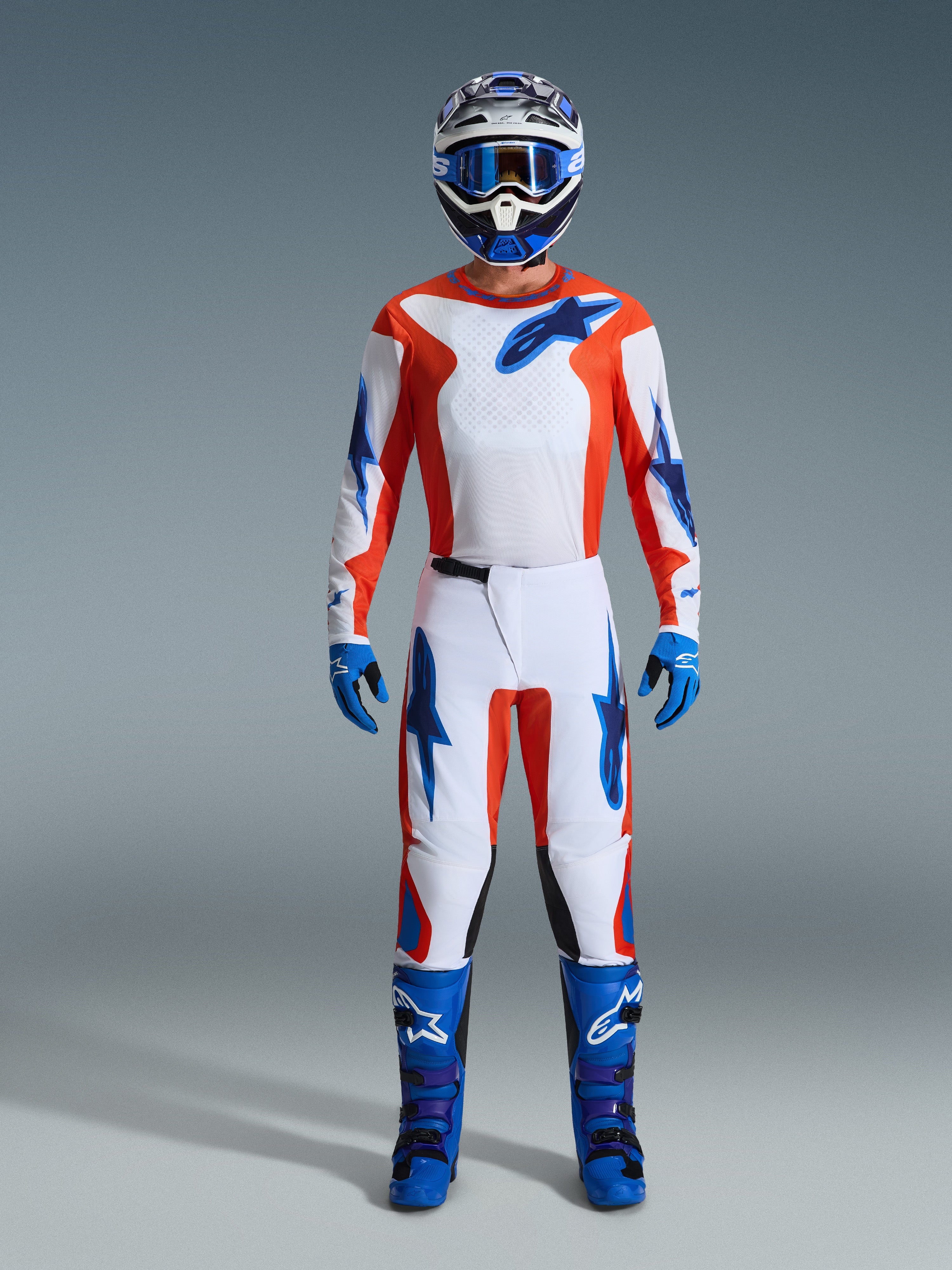 Alpinestars 2026 Fluid Grid Ausrüstungsset, Motocross-Fahrer in kompletter Ausrüstung, weißes Trikot und Hose mit Akzenten in Orange und UCLA-Blau, passender blau-weißer Helm mit blauer Schutzbrille, blaue Handschuhe und blaue Motocross-Stiefel, abgestimmtes Offroad-Rennoutfit