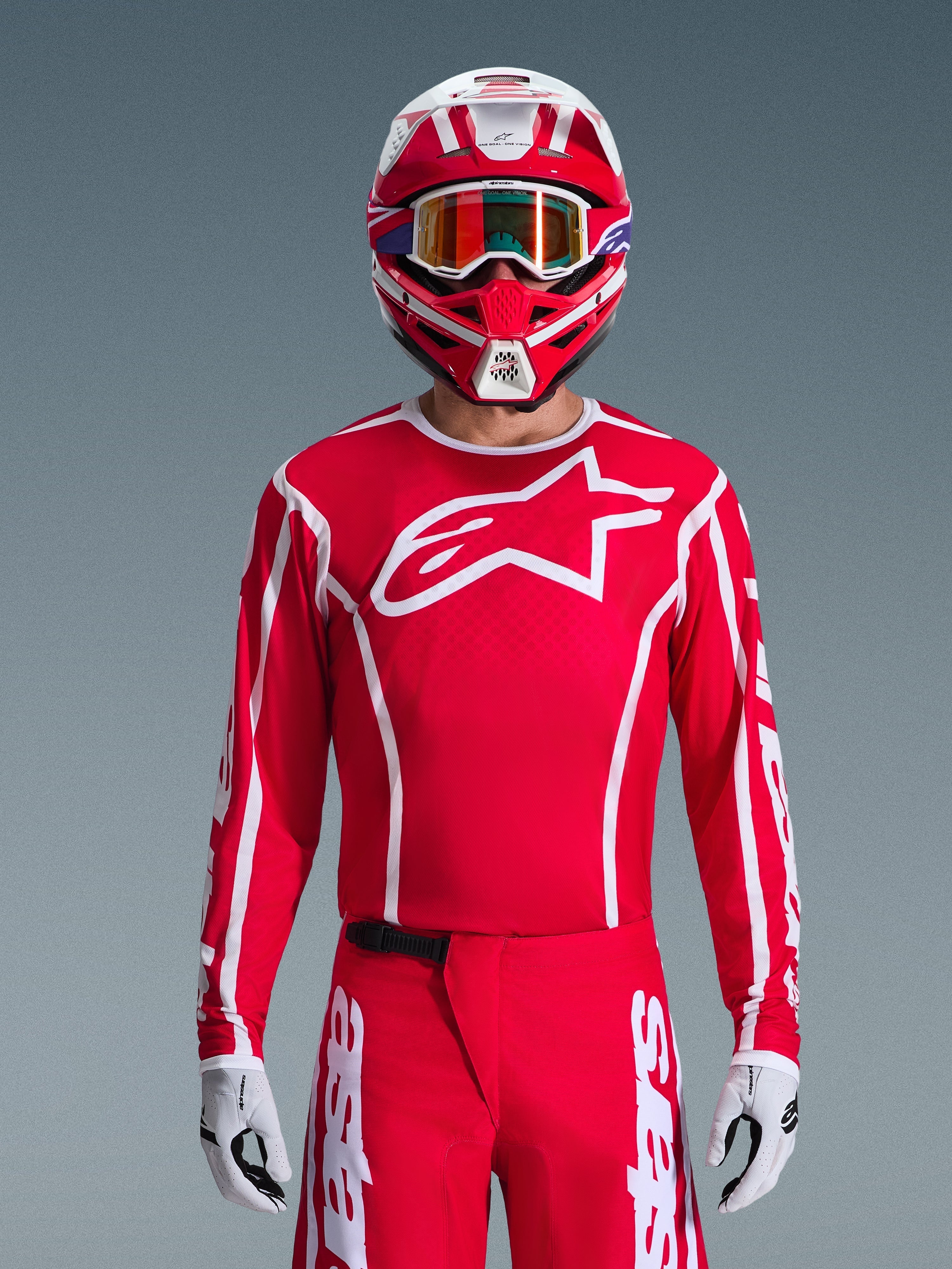 Alpinestars 2026 Fluid Apex Trikot, Motocross-Trikot, Rot und Weiß, getragen von einem Fahrer mit passendem rot-weißem Helm und orangefarbener Brille, mit markantem weißem Logo auf der Brust, sportliche Passform, Teil einer abgestimmten Offroad-Rennausrüstung