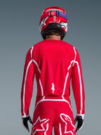Rückansicht eines Motocross-Fahrers im Alpinestars 2026 Fluid Apex Trikot in Rot und Weiß, mit geometrischen weißen Mustern, kombiniert mit passender Motocross-Hose und einem roten Helm, komplette Rennausrüstung für Offroad-Performance.