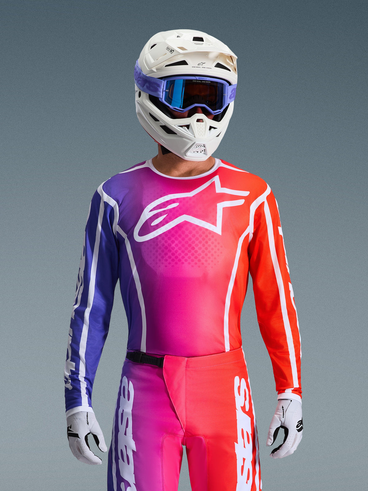 Motocross-Fahrer im 2026 Fluid Apex Trikot, lebhaftes Design mit Farbverlauf in Lila, Pink und Orange, großes weißes Alpinestars-Logo auf der Brust, kombiniert mit weißem Helm, lila Goggles und weißen Handschuhen für einen kompletten Offroad-Rennlook.