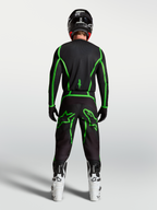 Alpinestars Fluid Apex V2 Trikot, Motocross-Ausrüstung, Schwarz und Leuchtgrün, Rückansicht am Fahrer mit weißen Stiefeln.