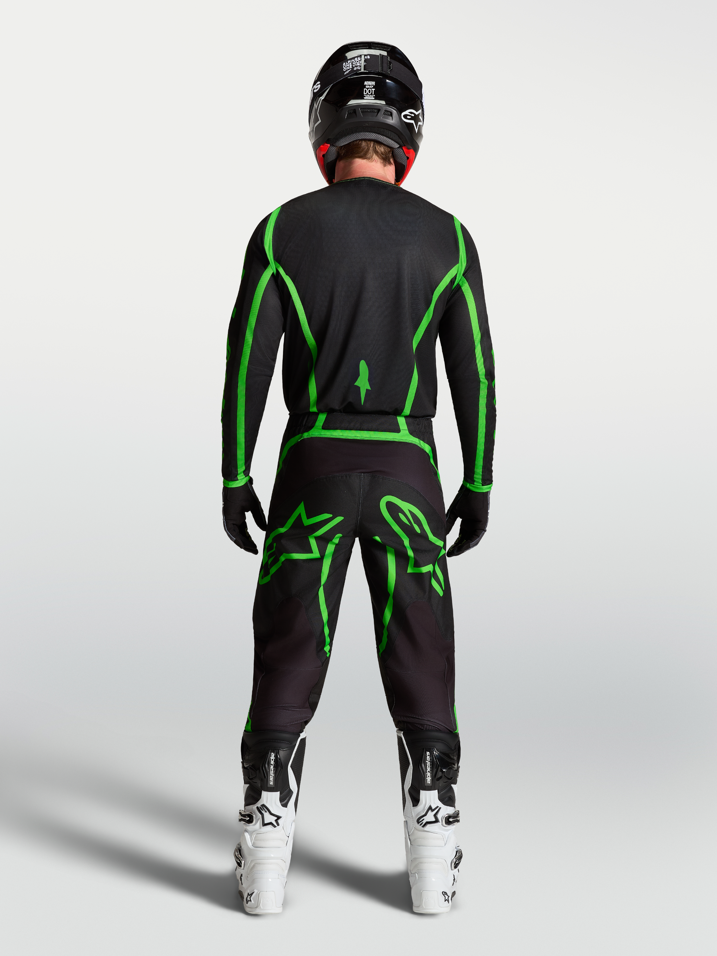 Alpinestars Fluid Apex V2 Trikot, Motocross-Ausrüstung, Schwarz und Leuchtgrün, Rückansicht am Fahrer mit weißen Stiefeln.