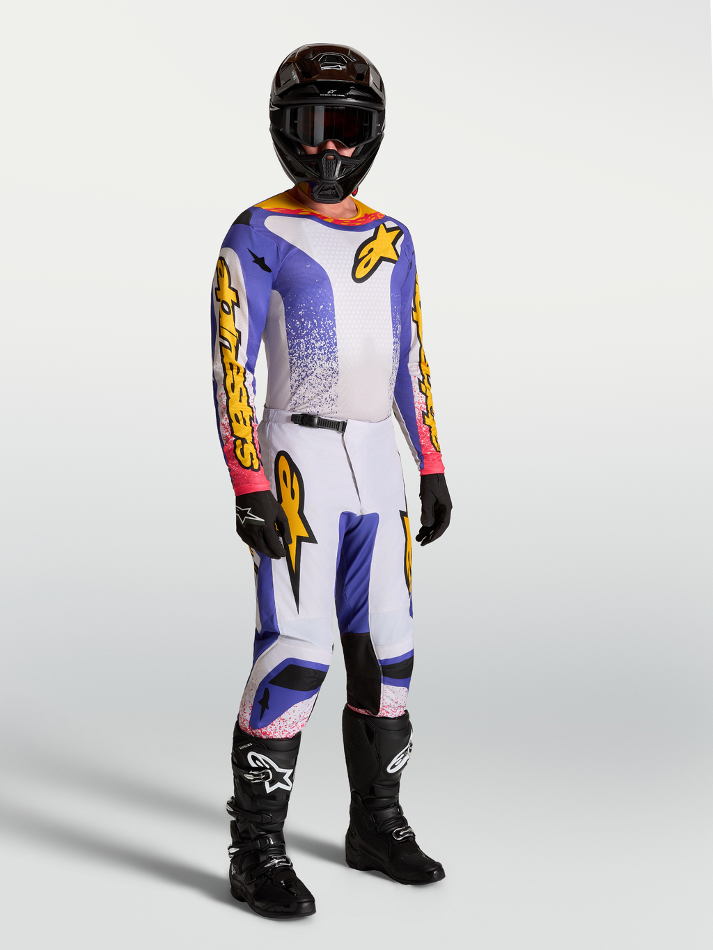 Alpinestars Fluid Drag Trikot und Hose, Herren-Motocross-Set in Blau, Weiß und Lila mit schwarzen Stiefeln und Helm.