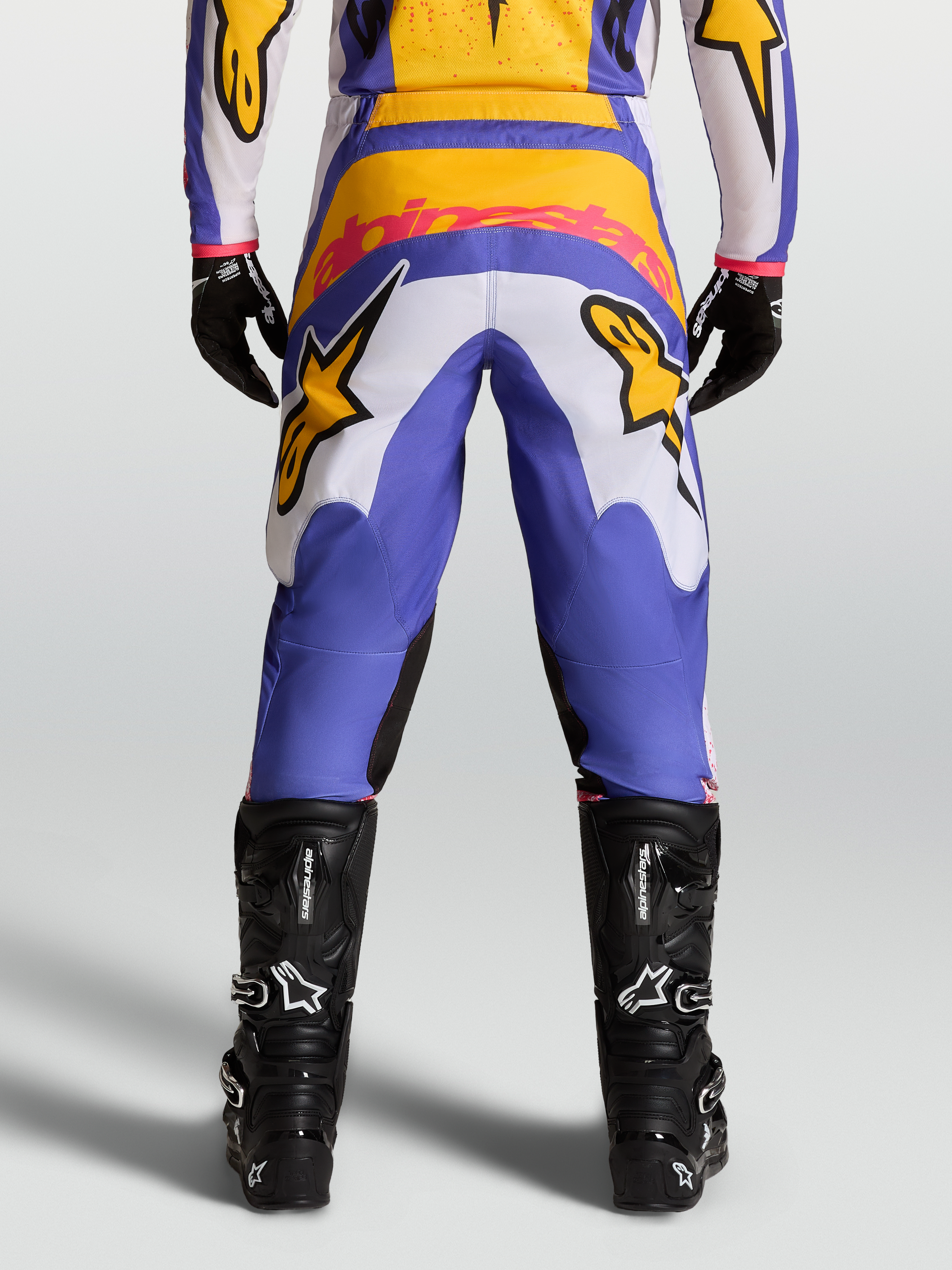 Alpinestars Fluid Drag Hose, Motocross-Hose in Blau und Gold, Rückansicht mit verstärktem Sitz, Stretch-Cord-Einsätzen und schwarzen technischen Stiefeln.