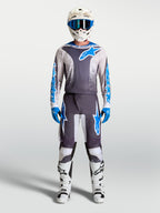 Alpinestars Fluid Drag Jersey in Graystone and Blue, worn as a motocross kit with a matching white helmet and racing boots.