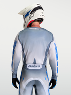 Alpinestars Racer Amber Trikot, Motocross-Trikot in Aschgrau und Weiß, rückseitige Modellansicht mit weißem Helm, ergonomische Passform für Offroad-Rennen