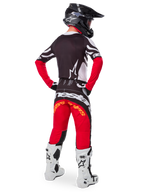 Alpinestars Limited Edition Techstar Deep Gear Set, Rückansicht eines Motocross-Fahrers, schwarzes Trikot mit weißen und roten Akzenten, passende rot-schwarze Hose mit Alpinestars-Branding, weiße Rennstiefel und schwarzer Helm, komplette Offroad-Rennausrüstung