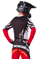 Motocross-Fahrer von hinten mit dem Alpinestars Limited Edition Techstar Deep Jersey in Schwarz, Weiß und High Red, dazu die passende Rennhose und ein schwarzer Helm, athletische Passform für Offroad-Performance
