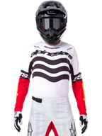 Motocross-Fahrer in kompletter Rennausrüstung, Limited Edition Techstar Deep Trikot in Weiß und Schwarz mit roten Ärmeln, wellenförmige Grafiken und markantes Alpinestars-Branding, weiße Motocross-Hose, schwarzer Helm und Brille, abgestimmtes Outfit für Offroad-Rennen