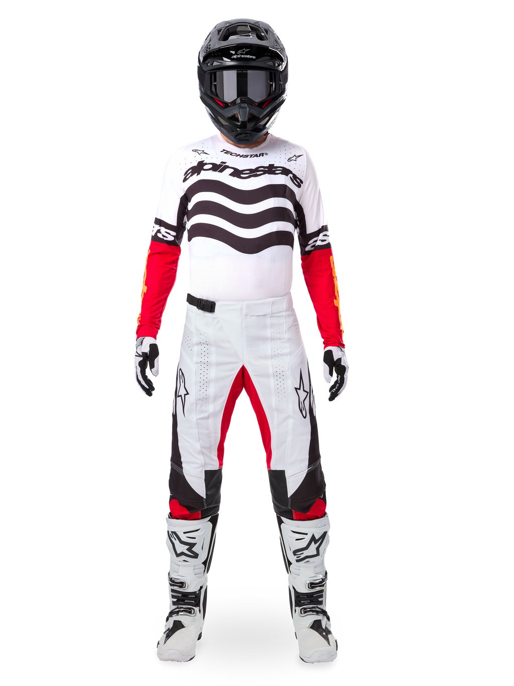 Motocross-Fahrer in der Alpinestars Limited Edition Techstar Deep Ausrüstung, weißes Jersey mit schwarzen Wellengrafiken und roten Ärmeln, passende weiß-schwarze Hose mit roten Akzenten, schwarzer Helm mit dunkler Brille und weiße Stiefel, professionelles Offroad-Outfit