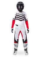 Motocross-Fahrer im Alpinestars Limited Edition Techstar Deep Trikot in Weiß, Schwarz und Rot mit wellenförmigen Grafiken auf der Brust, kombiniert mit einer passenden weiß-roten Hose, einem schwarzen Helm und weißen Rennstiefeln, komplette professionelle Offroad-Ausrüstung.