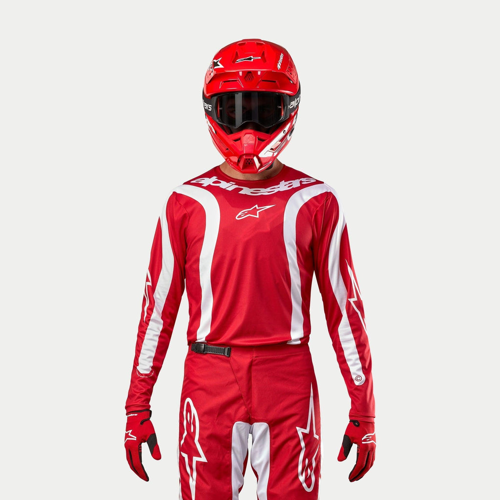 Alpinestars 2024 Fluid Lurv Trikot, Motocross-Trikot, Mars-Rot und Weiß, getragen mit passender roter Hose, Helm und Handschuhen, mit weißen Grafikakzenten an den Ärmeln und markantem Branding auf der Brust, athletische Passform für den Offroad-Rennsport