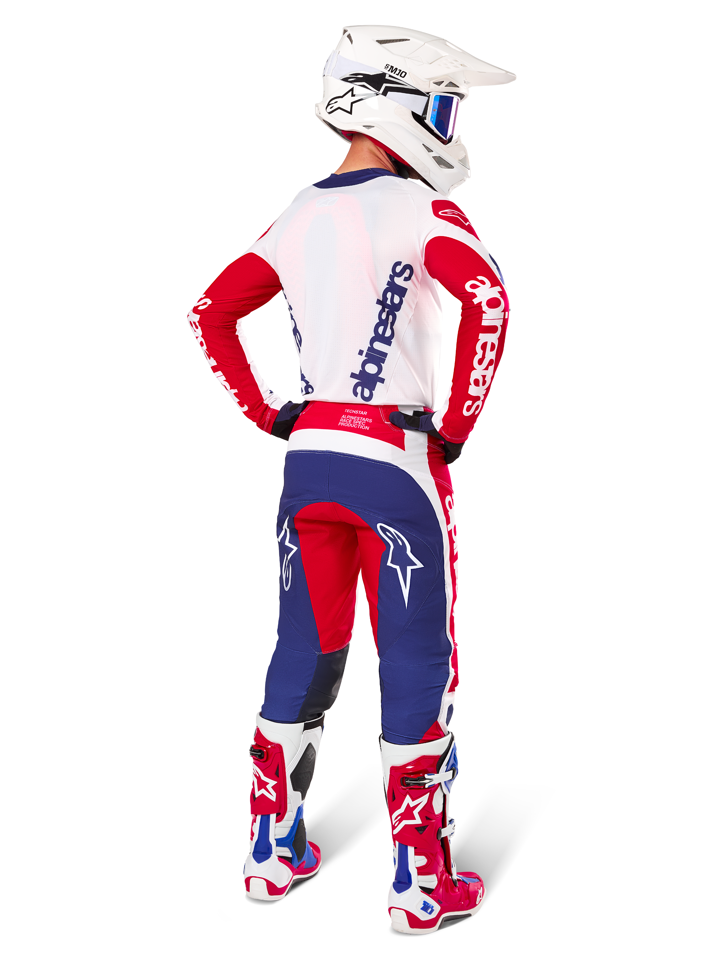 Motocross-Fahrer in der Rückansicht, Alpinestars Limited Edition Techstar Fortitude Jersey in leuchtendem Rot, Weiß und Blau, passende technische Hose mit Stern-Logos, weißer Helm mit Schutzbrille und rot-weiße Stiefel, komplette koordinierte Ausrüstung für Offroad-Rennen
